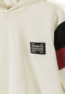 Close-up of cream hooded sweatshirt with black, red contrast sleeve panels and a small black patch design on chest.