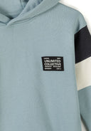 Close-up of blue hooded kids top with contrast sleeve panels and patch design detail on chest