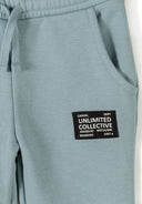 Close-up of blue hooded tracksuit pants featuring contrast sleeve panel design and a black patch with white text detailing.