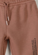 Close-up of cognac-colored kids' tracksuit pants with elastic waistband and motivational text design on leg