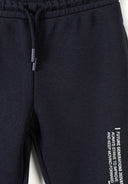 Close-up of black kids’ tracksuit pants with elastic waistband, drawstring, and motivational white printed text design.