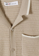 Detail of a beige knitted polo shirt with a classic collar and button fastening.