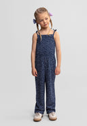 Young girl wearing a navy blue patterned sleeveless jumpsuit with casual sneakers and braided hair bows on each side