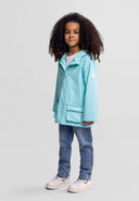 Young girl with curly hair wearing a mint waterproof jacket with adjustable cuffs and casual jeans standing confidently