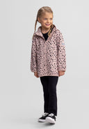Smiling girl wearing a pink softshell jacket with black spots, paired with black pants and sneakers, showcasing a stylish kids design.