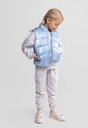 Young girl wearing metallic light blue quilted waistcoat with stand collar and zip fastening, hands in side pockets, kids fashion design.