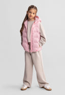 Young girl modeling a lightweight pink nylon gilet with hood and side pockets, styled with casual neutral outfit.