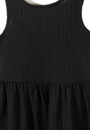 Close-up of black sleeveless girls dress with textured tiered design and adjustable back fastening details.