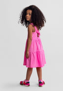 Young girl wearing a pink sleeveless tiered dress with adjustable back drawstring and casual sneakers standing sideways