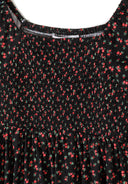 Close-up of black fabric with red floral print and shirred bodice design on girls dress.