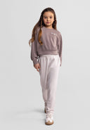 Young girl wearing a brown crew neck sweatshirt with embroidered design and light-colored pants in a casual pose