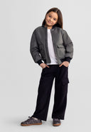 Young girl wearing black wide leg joggers with combat pockets and a stylish jacket, showcasing modern kids fashion design.