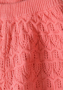 Close-up of coral pink crocheted fabric showcasing intricate knit design suitable for girls' clothing in kids fashion.