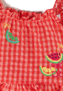 Close-up of orange gingham fabric with colorful fruit embroidery design on kids’ cotton blend clothing.