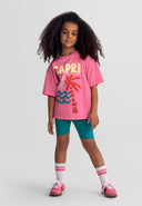 Girl wearing pink graphic top and teal shorts, showcasing kids fashion with a playful summer activewear design