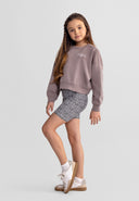 Young girl modeling short cycling leggings with animal print design and a casual sweatshirt in a studio setting