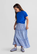 Young girl wearing a blue floral maxi skirt with elasticated waistband, paired with a blue top and sneakers.