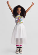Young girl wearing an off-white pleated tulle skirt with cheerful flowers on her top, raising arms joyfully