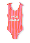 Pink coral striped girls swimsuit with adjustable straps and bow details featuring fun Palm Springs text design