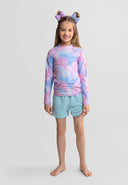 Smiling girl wearing a long sleeve pink and blue gradient rash vest with blue shorts and hair bows