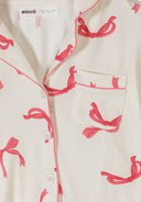 Close-up of white fabric with pink bow print, lapel collar, button front, and chest pocket detailing in kids fashion design.