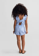 Girl wearing a blue floral short sleeve jumpsuit with ruffle details and a bow back design, showcasing kids fashion.