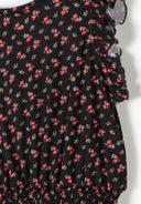 Close-up of black fabric with red floral print and delicate ruffle detailing on short jumpsuit design for girls.