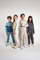 Four children model coordinated, soft-textured sweatshirt and jogger sets in muted tones of blue, beige, gray, and cream.