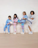 Four children in tie-dye sweatshirt and pants sets pose playfully against a marble wall.