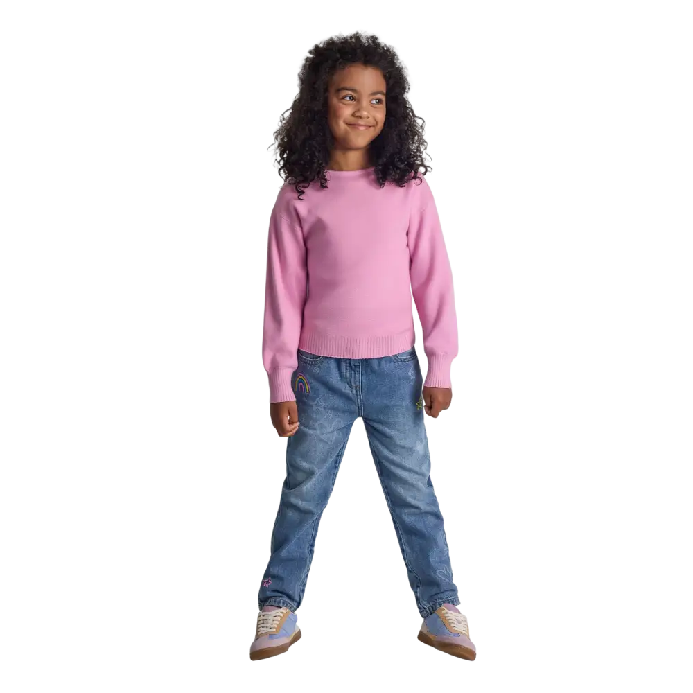 Young girl wearing pink textured knit jumper with boat neckline and blue jeans, full body view on black background