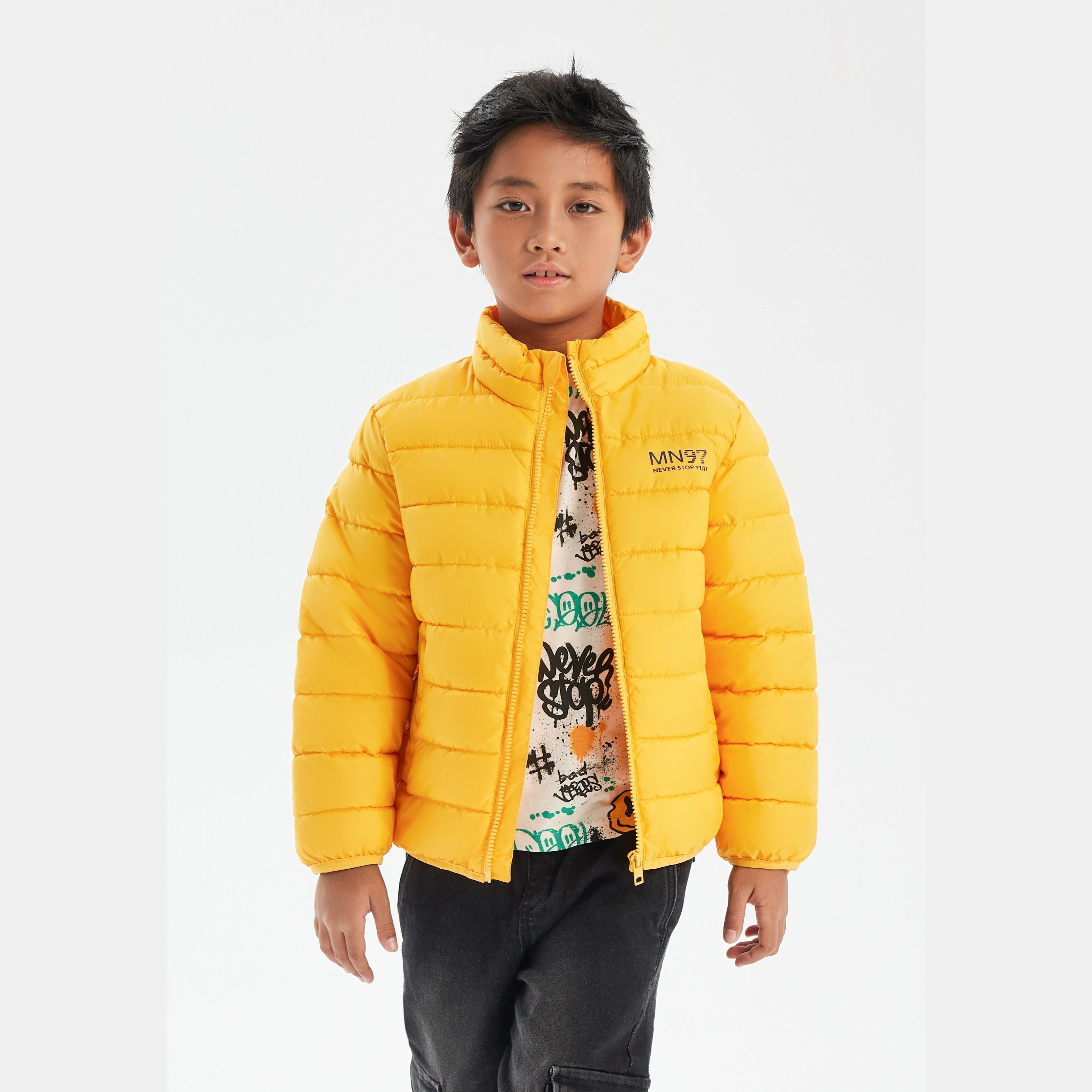 Close-up detail of yellow jacket showing zip closure, Minoti brand label, and quilted padding texture